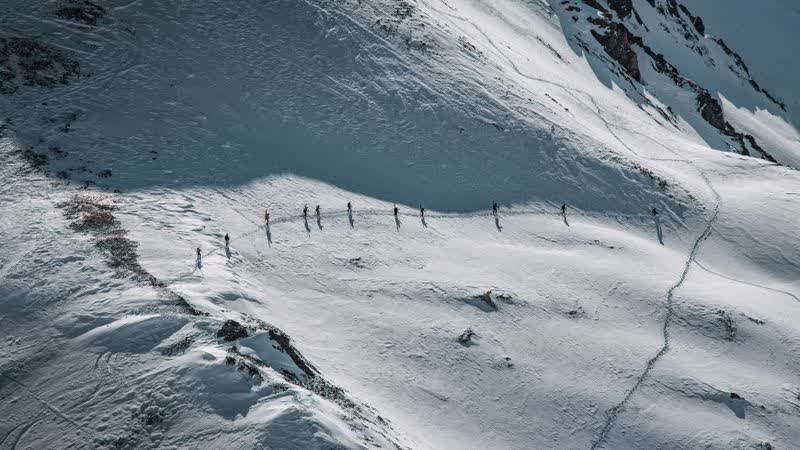 Skitourengruppe zieht in einer Reihe über einen verschneiten Hang