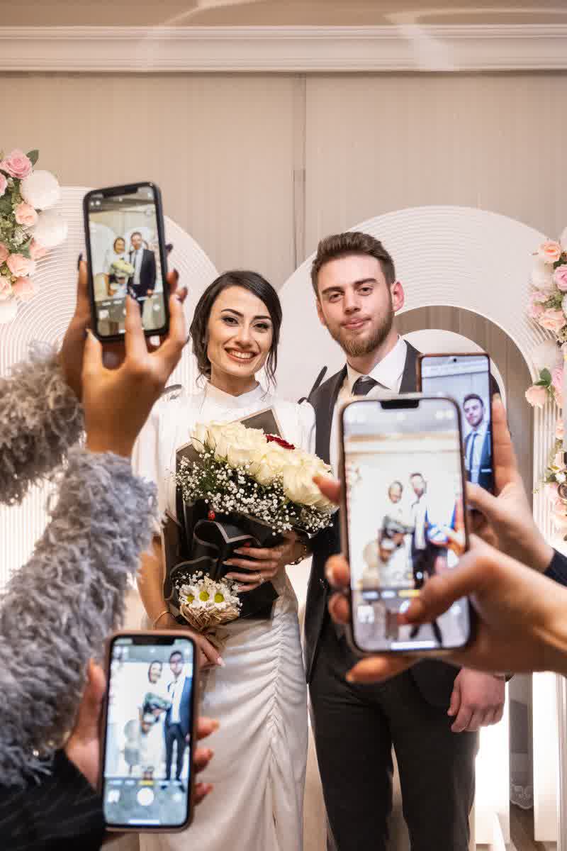 Hochzeitsgäste halten vier Handys auf das Brautpaar, auf jedem Display dasselbe Bild