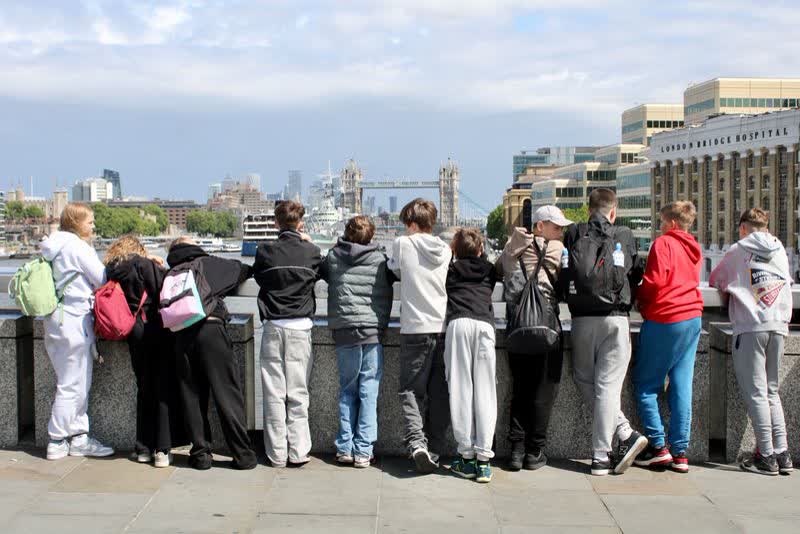Schulklasse steht von hinten am Themseufer und schaut zur Tower Bridge