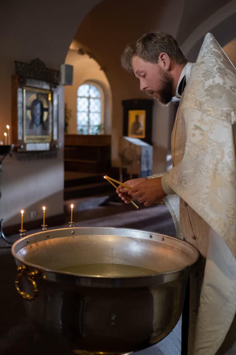 Geistlicher entzündet die Kerzen am Taufbecken einer Kirche